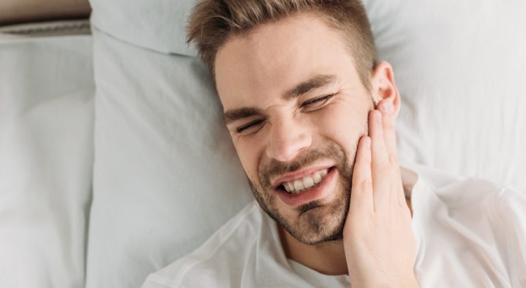 top view of young man touching cheek while suffering from toothache