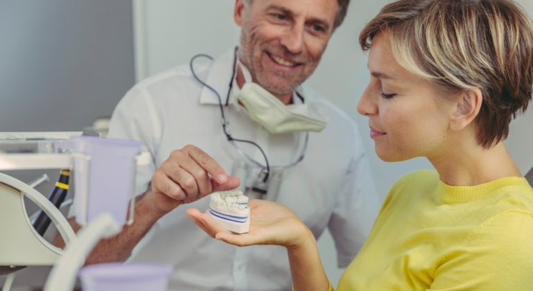 Dentist explaining dental bridg on a tooth model to his patient